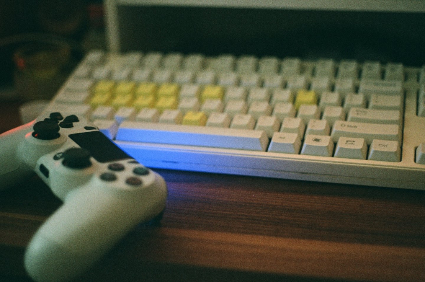 A white game controller rests beside a keyboard on a wooden desk.